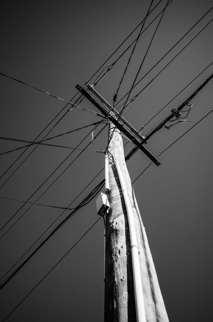 Monochrome low-angle shot of a power pole and wires against a clear sky.